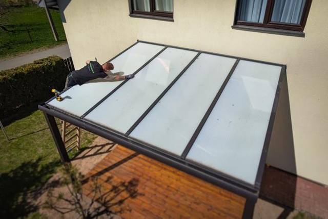 Aluminium patio cover with opal roof panels being fitted above a timber deck